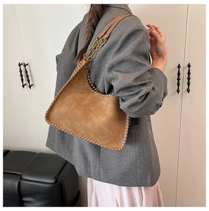 Detailed side view of brown suede shoulder bag with woven edges and gold chain strap