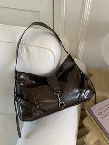 Dark brown patent leather hobo bag with silver buckle in a minimalist home setting