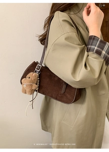 Detail of dark brown suede baguette bag with plush bear charm and adjustable strap