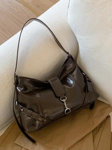 Chocolate brown dumpling bag with metallic buckle and adjustable strap on white sofa