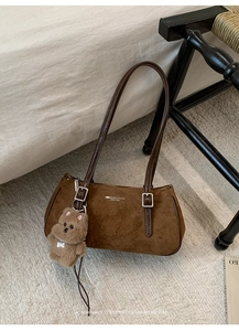 Close-up of brown suede baguette bag featuring fashion logo and a cute teddy bear charm