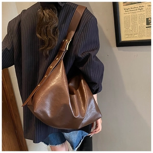 Brown leather hobo bag with adjustable gold buckle shown on shoulder in a stylish setting