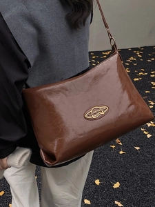Large brown leather tote bag with gold logo shown on an autumn street setting