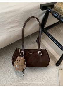 Detail of dark brown suede baguette bag with silver hardware and a plush bear charm