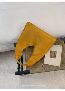 Detail of a ginger yellow suede tote bag with a minimalist half-moon shape on a chair
