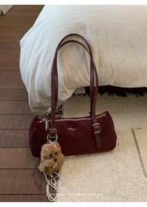 Detail of burgundy suede shoulder bag featuring silver zippers and a cute plush bear charm