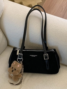 Retro black suede baguette underarm bag with a cute dog plush charm on a sofa