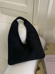 Minimalist black matte large capacity hobo bag leaning against a soft white sofa