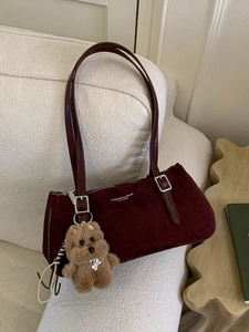 Retro burgundy baguette shoulder bag with plush bear pendant on a white fabric sofa