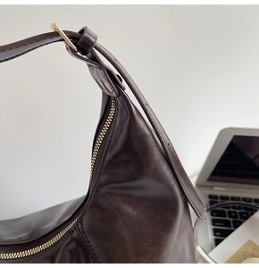Detail einer dunkelbraunen Hobo-Tasche aus Leder mit goldenen Beschlägen und Gurt