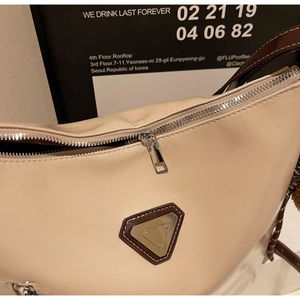 Detail of cream shoulder bag featuring silver zipper and brown leather trim on poster