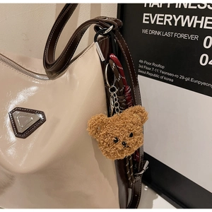 Detailed close-up of a brown teddy bear plush charm hanging on a beige leather tote bag