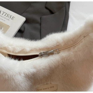 Gros plan sur le sac bandoulière en peluche blanc cassé avec fermeture éclair et texte