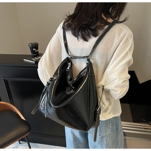 Detail of minimalist black glossy hobo backpack with white stitching and metal logo plate