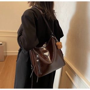 Detail of dark brown glossy patent leather tote bag with silver hardware and bear charm