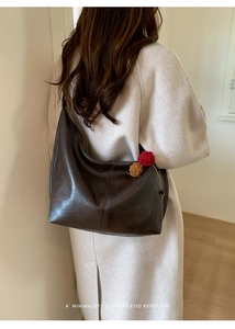 Detail of dark brown leather tote bag with knit pendant on beige minimalist coat