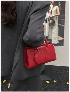 Detailed view of a red textured leather handbag with a round charm on a grey blazer outfit