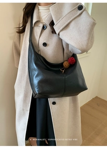 Detail view of black leather hobo bag on shoulder with decorative brown pom-pom charm