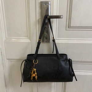 Detail of black faux leather shoulder bag with gold buckles and vintage beaded charm