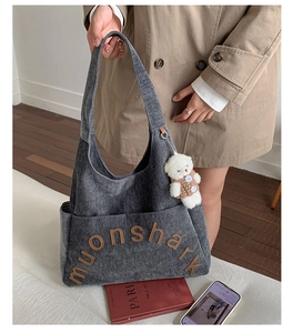 Détail d'un sac cabas en maille grise avec poche avant et breloque ours en peluche