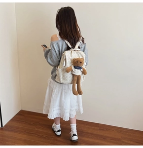 Detail of cute off-white canvas backpack with a plush bear charm on the back