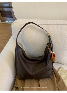 Brown leather hobo bag with retro charm featuring creative woven tassels on a soft white sofa