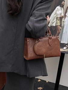 Retro brown leather square tote bag with round charm shown held by a model in a grey coat