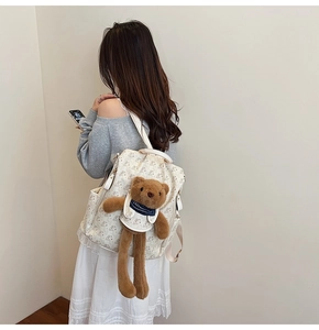 Close-up of minimalist cream backpack with bear patterns and plush bear charm on model