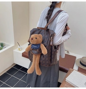 Detail of dark brown backpack featuring teddy bear prints and a plush bear charm