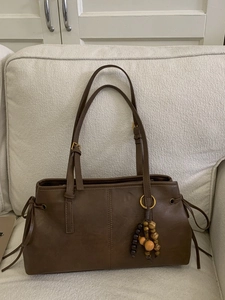 Retro dark brown leather tote bag with vintage wooden gourd charm on a soft sofa