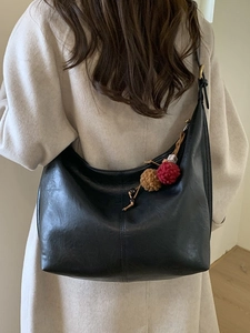 Black leather crescent tote bag with colorful pompom charm on a model in a long coat