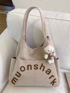 Sac fourre-tout en velours côtelé beige avec lettres 3D et breloque ours sur un canapé
