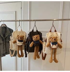 Three minimalist backpacks with vintage bear patterns and plush bear charms hanging on a rack