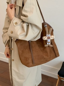 Large brown suede tote bag with checkered accent and bunny charm on model in a trench coat