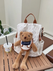 Cute white mini backpack with brown bear pattern and plush bear charm on wooden table
