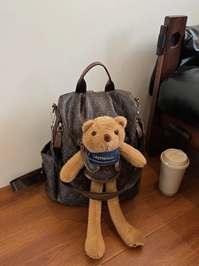 Brown monogram backpack with bear print and plush toy charm on wooden background