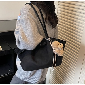 Close-up of black matte tote bag with a cute brown plush bear charm and thin shoulder straps