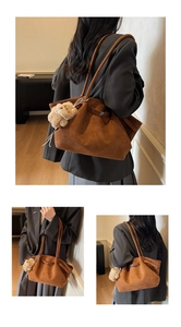 Détail d'un sac cabas marron mat avec deux fines poignées et un charm d'ours en peluche