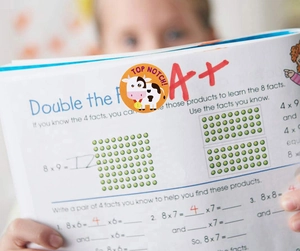 Close-up of cartoon cow reward sticker and A+ mark on a child's math workbook page