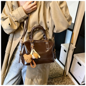 Detalle del bolso tipo doctor en cuero marrón oscuro con colgante de osito y asas superiores
