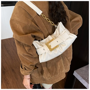 Detail of white pleated shoulder bag featuring a large gold buckle and metal chain strap