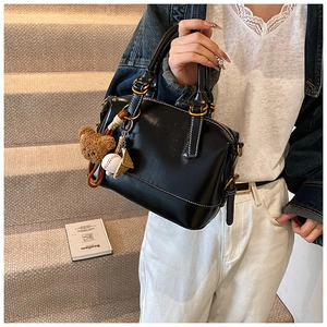 Detalle de bolso negro brillante con oso de peluche y colgantes decorativos