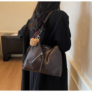 Detail of dark brown leather tote bag with long tassel zipper and plush bear pendant