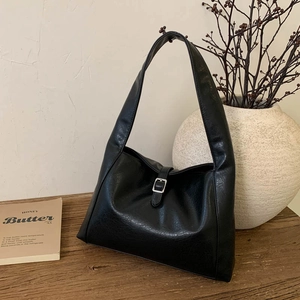 Detail einer schwarzen Halbmond-Tasche mit Silberschnalle auf einem Holztisch