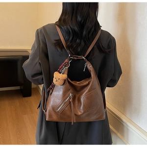 Brown leather Hobo bag with plush bear charm shown in a cozy indoor lifestyle setting