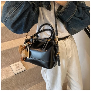 Detalle de un bolso Boston negro brillante con colgantes y correa ajustable