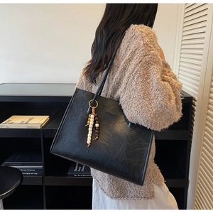 Detail of a large black leather tote bag featuring a beaded tassel and shoulder strap