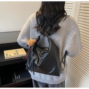 Detail of black soft leather backpack with bear pendant and stylish red plaid ribbon