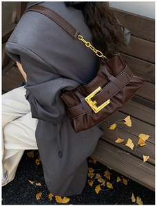 Detail of dark brown ruched shoulder bag with a large gold buckle and metal chain strap