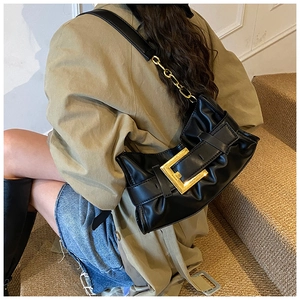 Detail view of black pleated cloud bag with large gold buckle and thick chain strap